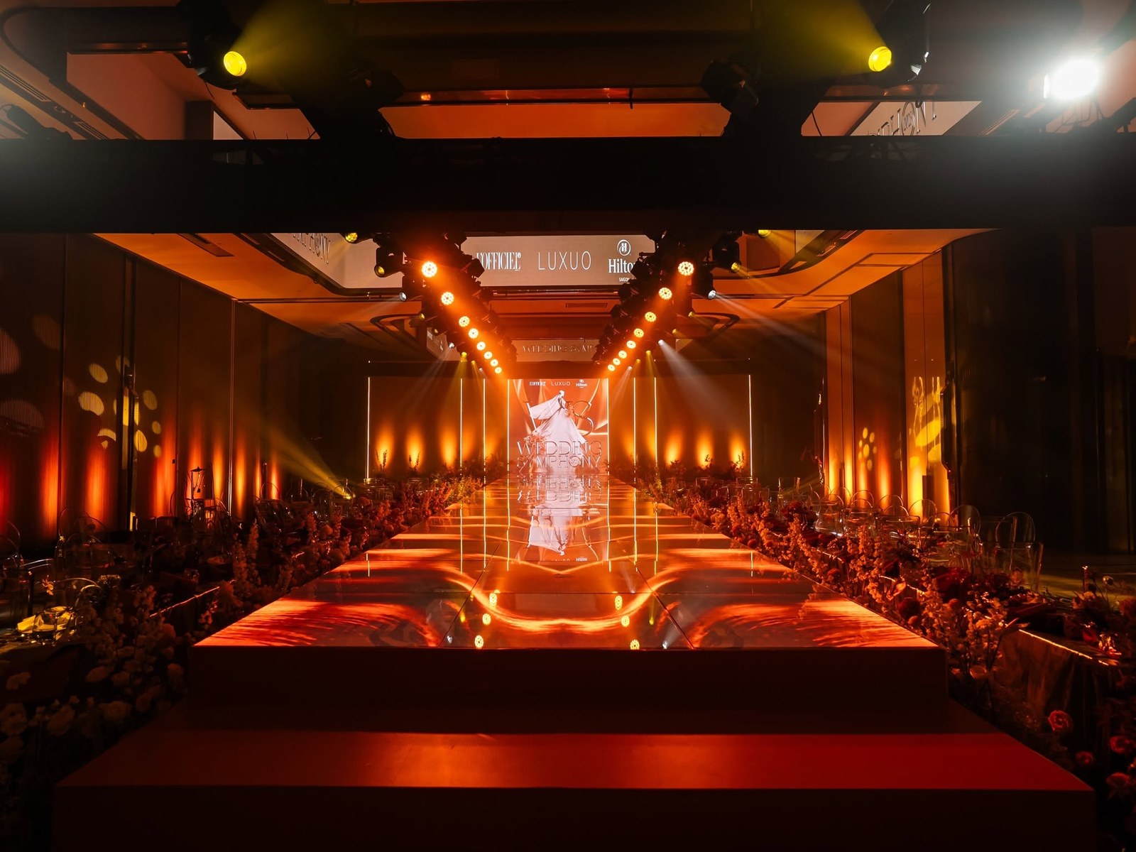 Wedding Symphony 2025 tại Hilton Saigon — sàn runway lung linh, hai bên là ghế ONE CHAIR trong suốt hoà quyện cùng hoa tươi